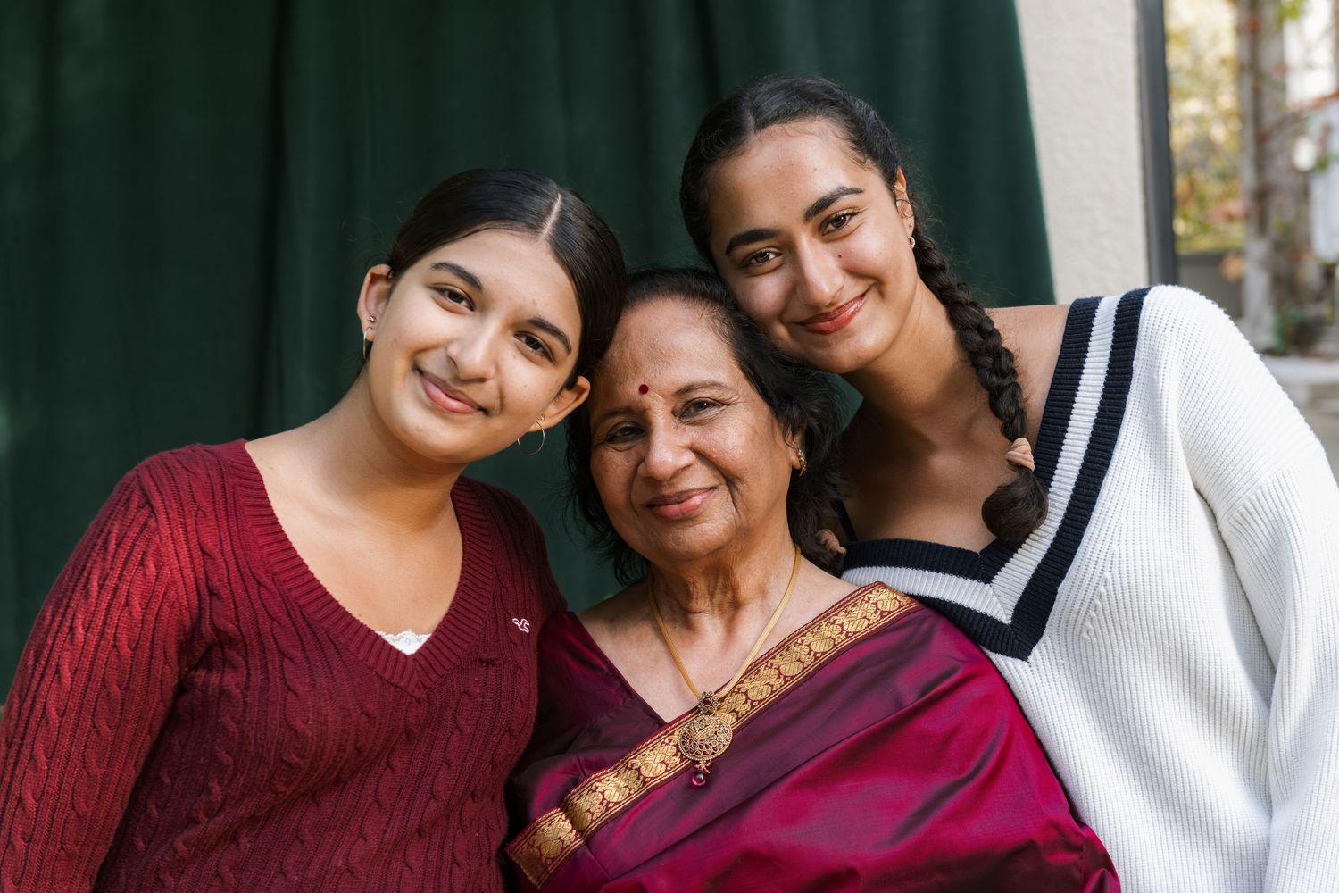 Three generations of Indian women smile together, with the elder wearing a traditional saree.
