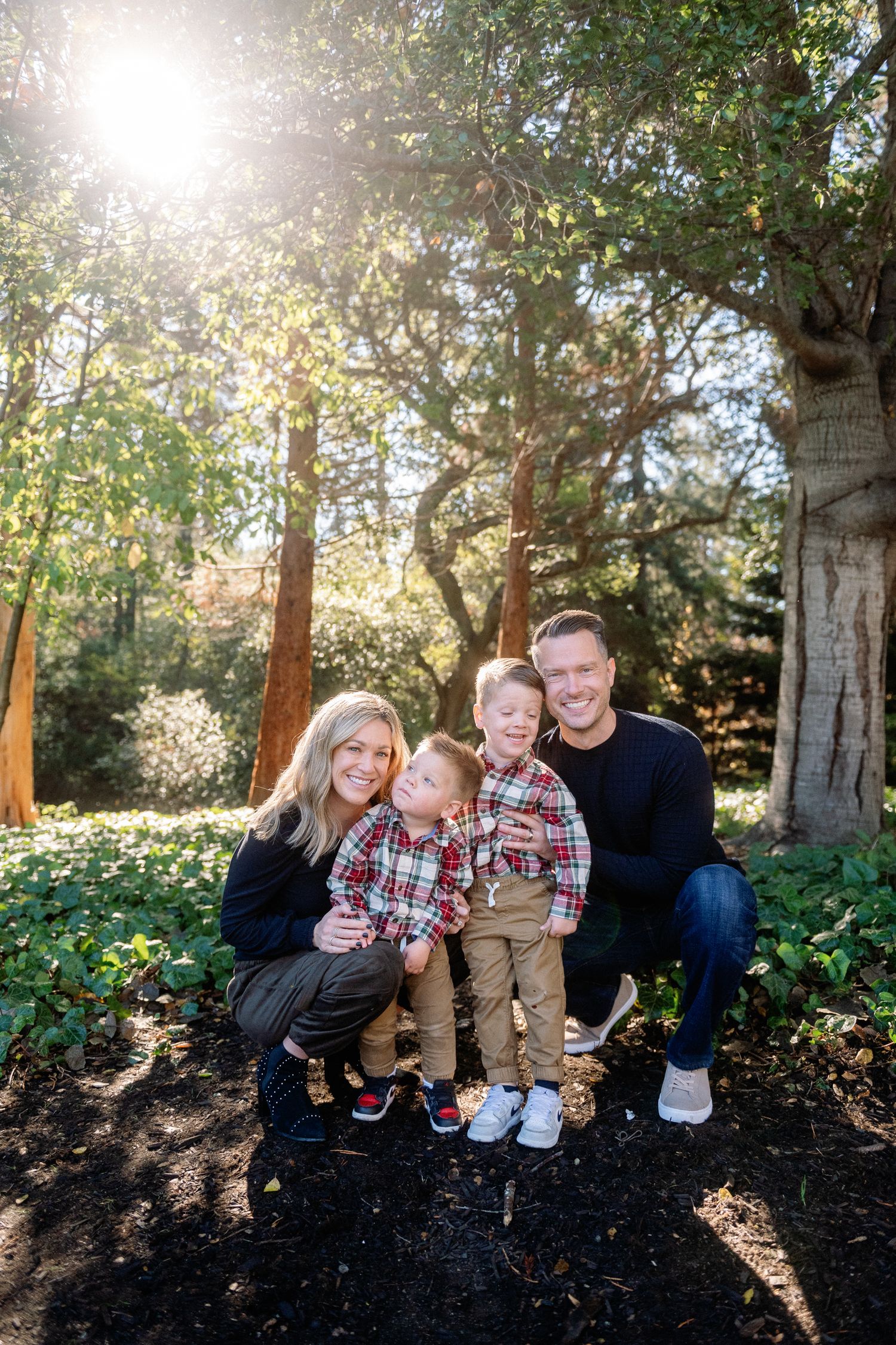 Family sitting together on a wooden bench in a sunlit forest setting with autumn foliage.