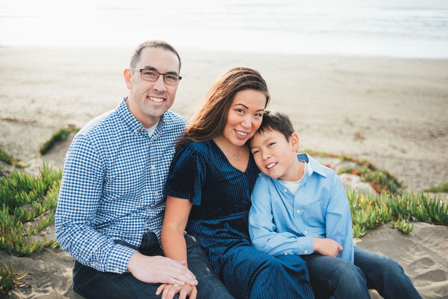 A family sits together on coastal rocks during a beach photoshoot.