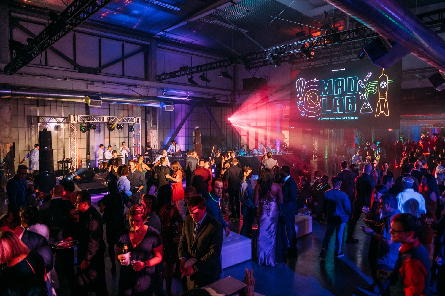 A crowded nightclub event space with colorful purple and red lighting illuminating the dance floor and party atmosphere.