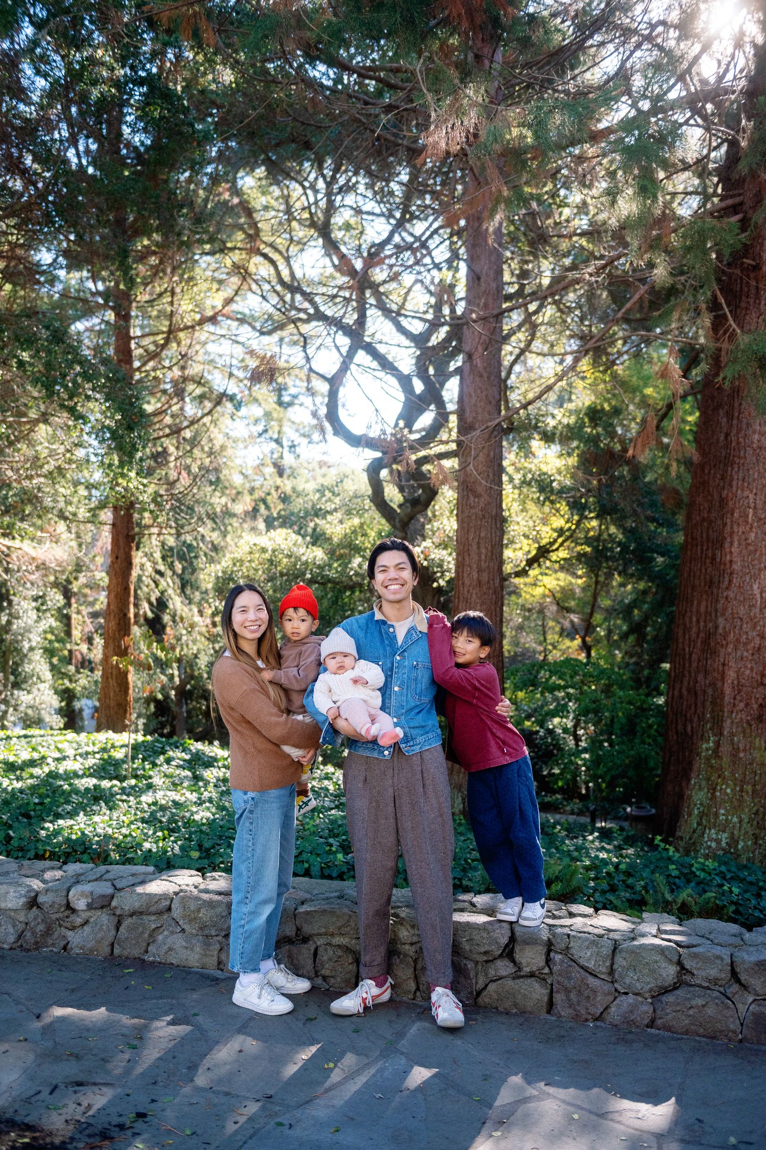Group photo session in a sunlit forest with stone wall backdrop.