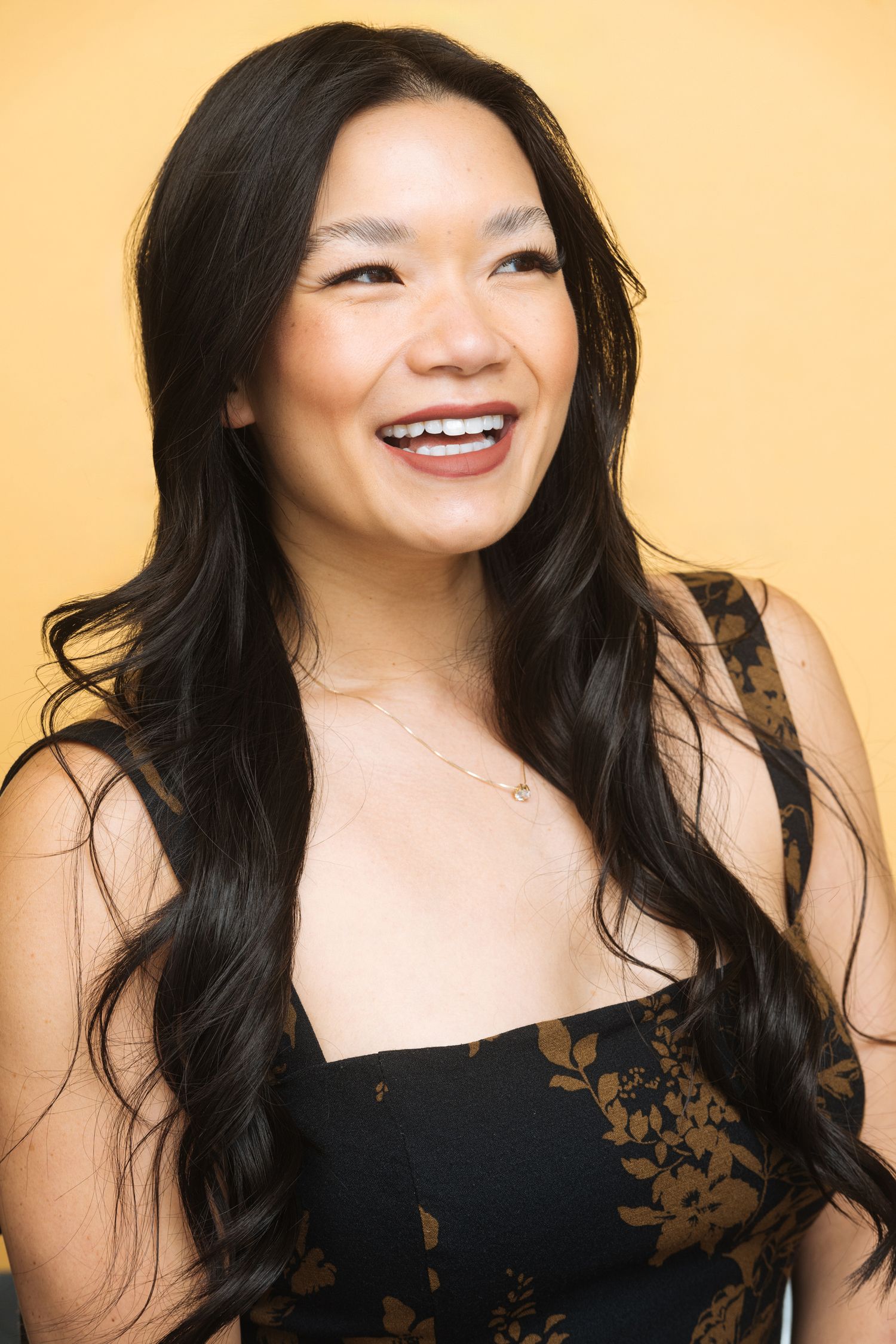 Studio portrait against yellow background with long dark hair and black top.