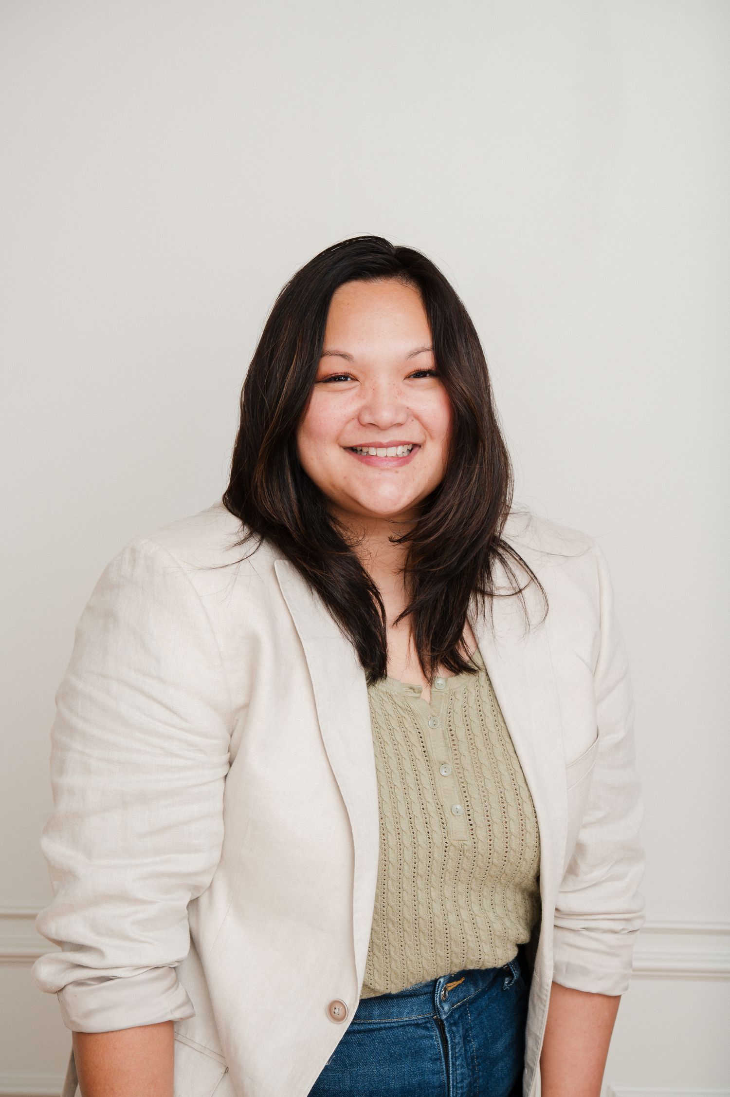 Smiling woman in a white blazer and green top poses confidently against a light background.