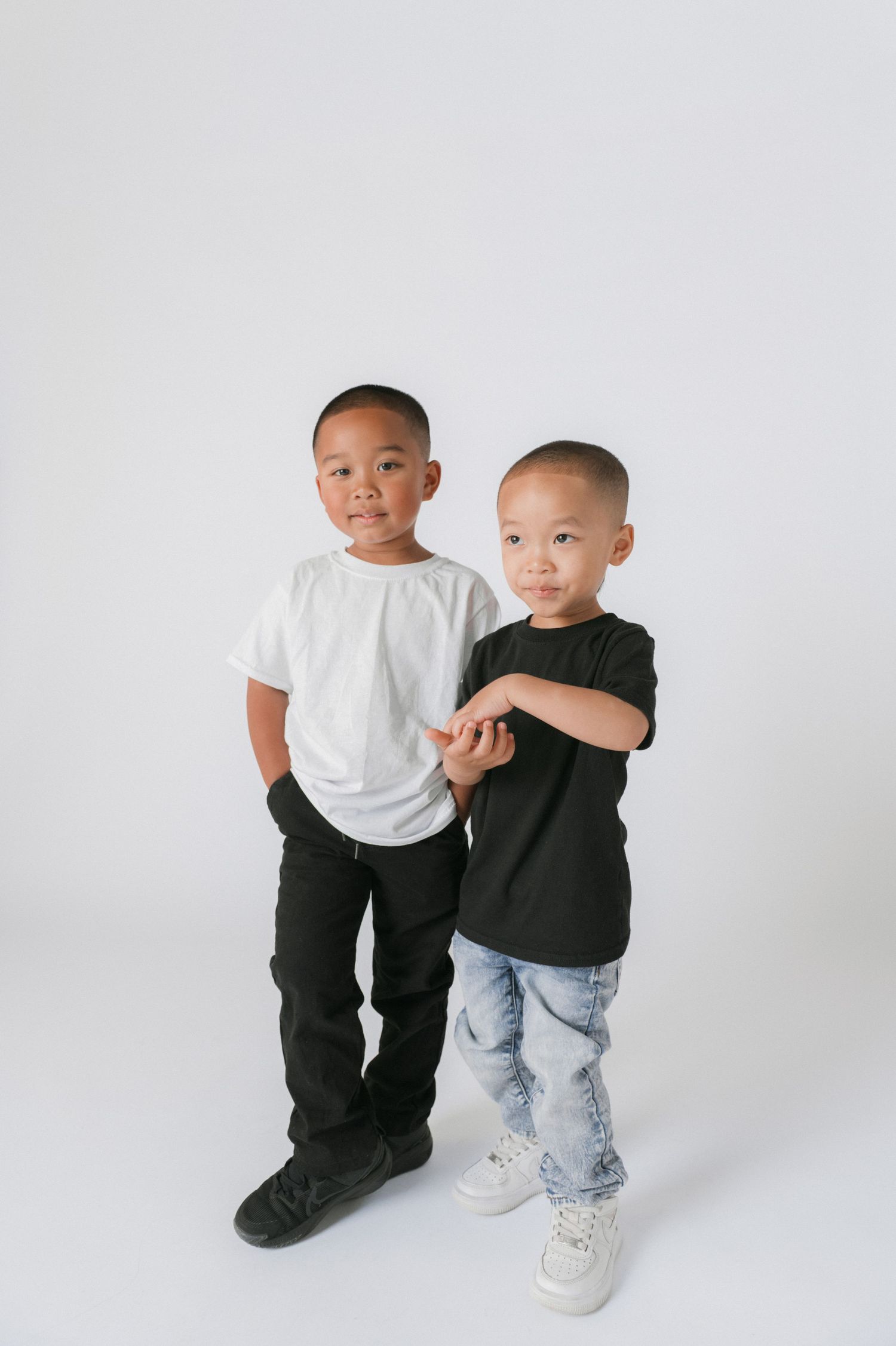 Two young boys in white and black t-shirts pose together against a white background.