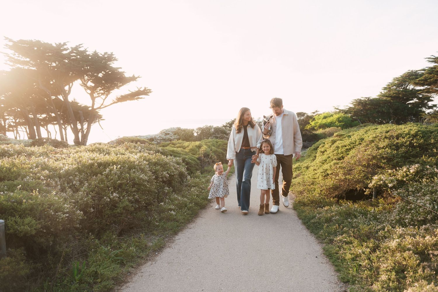 Family walking together on a coastal path during golden hour with trees in background.