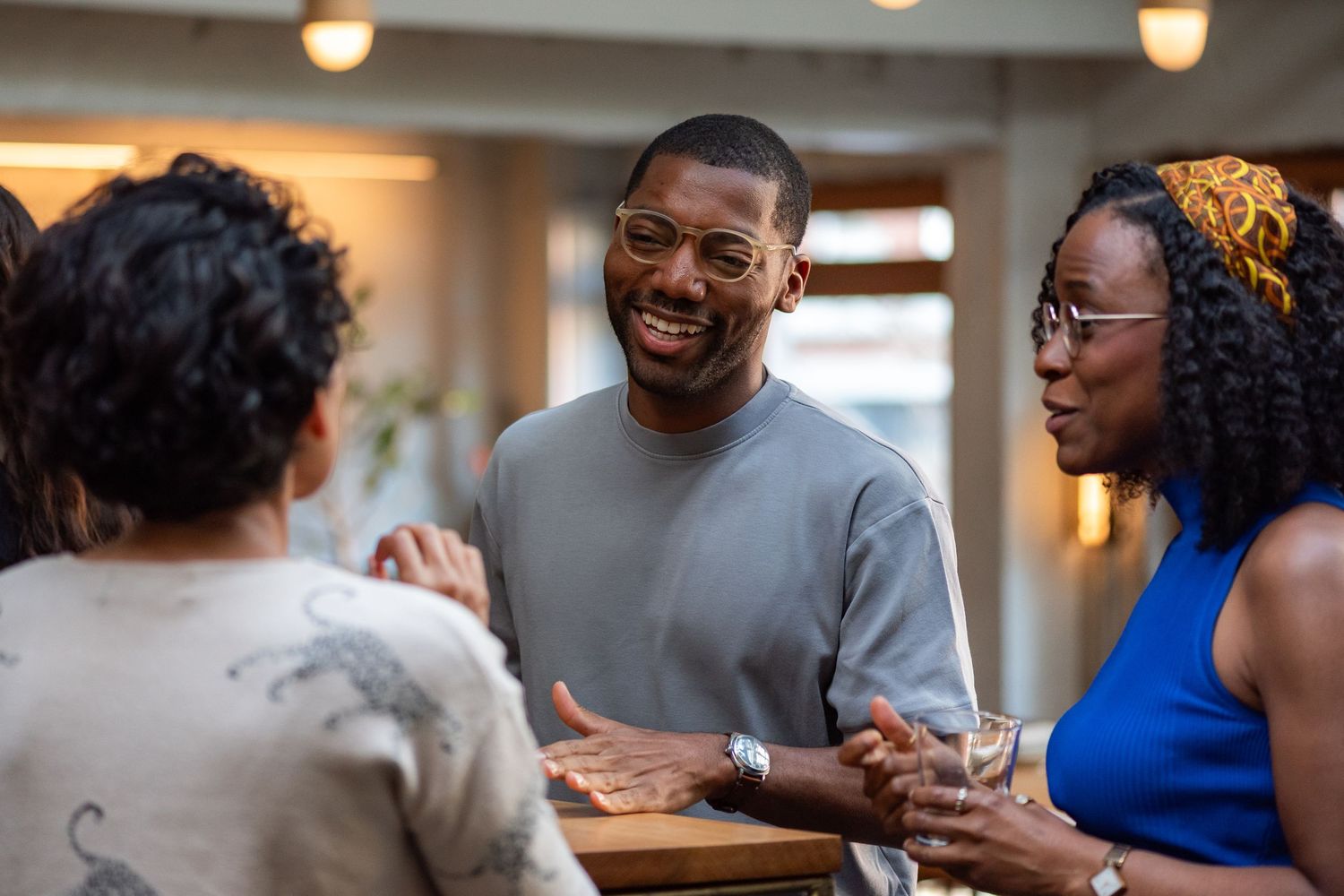 A group of friends share a lighthearted conversation while gathered around a table indoors.