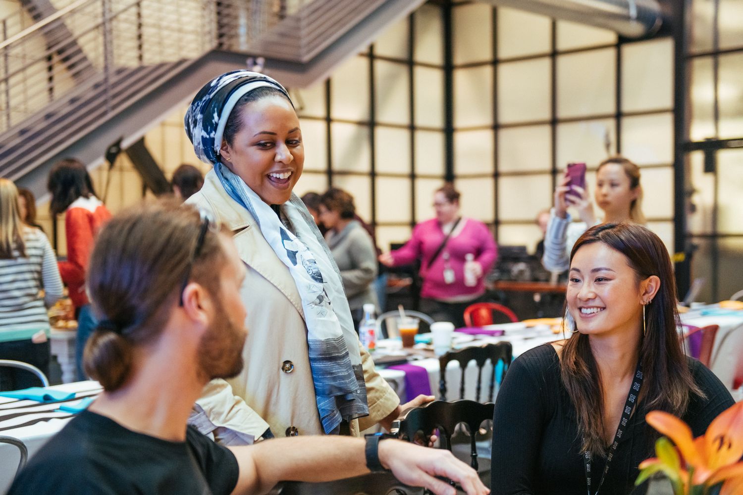 Three people smiling and conversing at a lively indoor networking event with colorful decorations in the background.