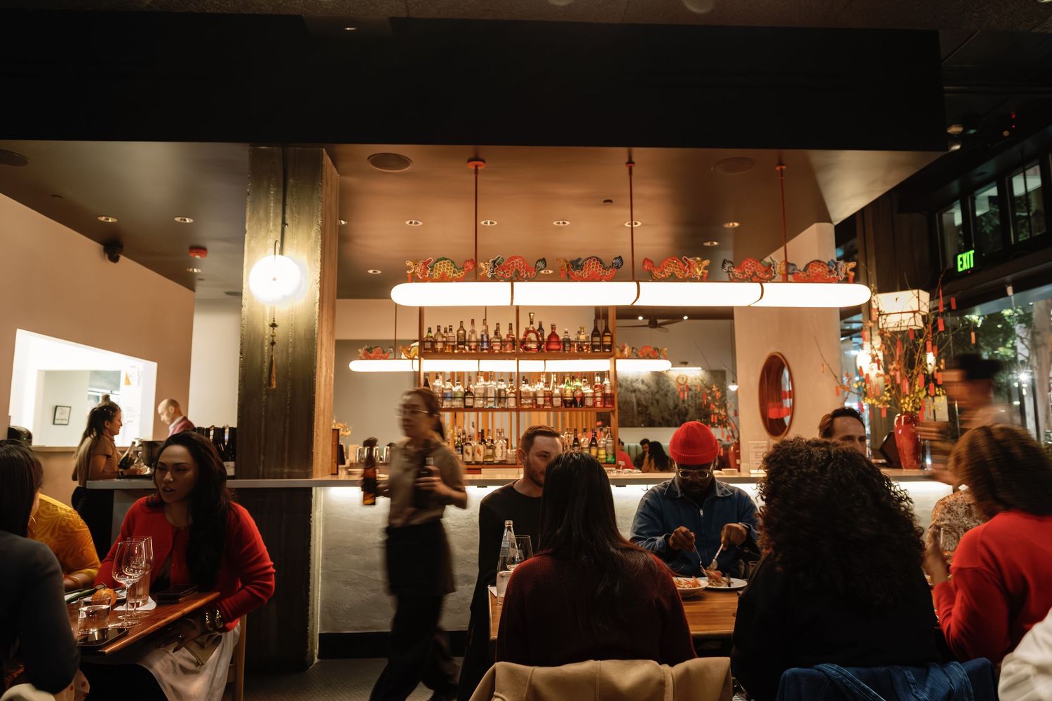 Busy restaurant bar with warm lighting, colorful decor, and diverse patrons enjoying drinks and conversation.