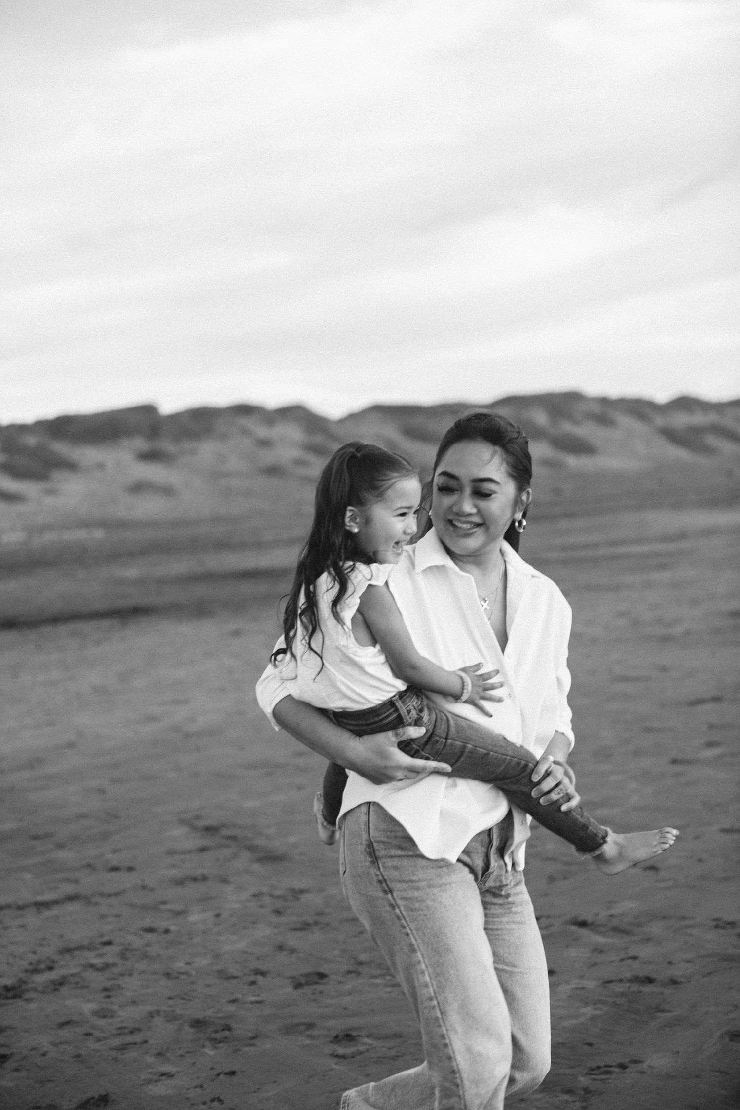 Black and white photos of a parent and child playing and embracing together on a sandy beach.