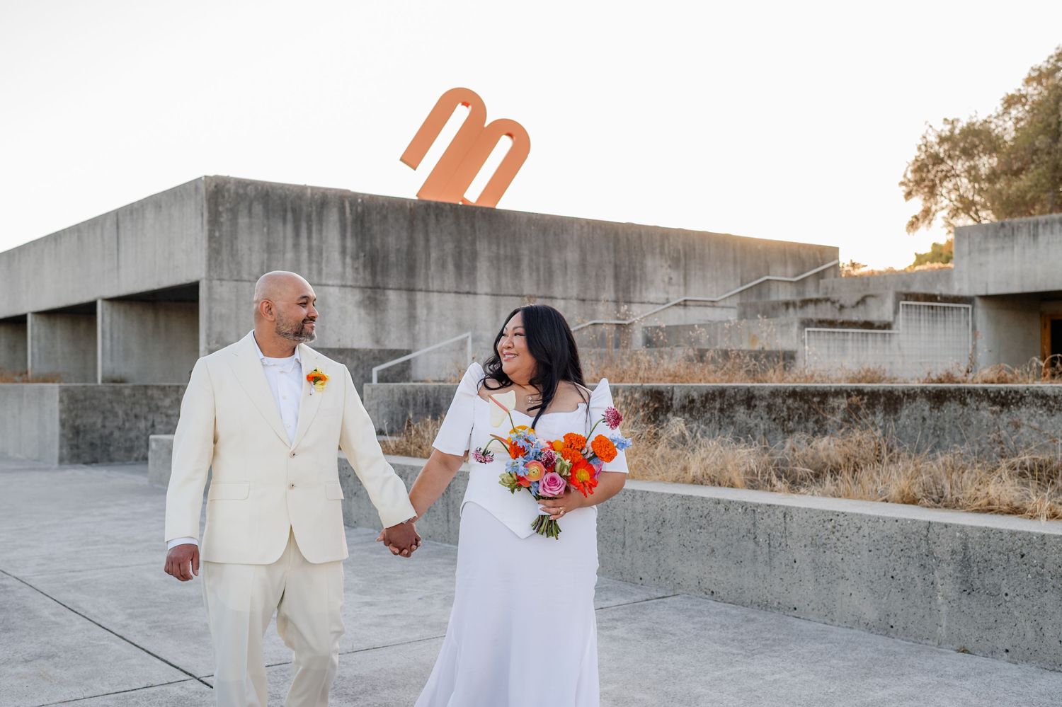 Wedding couple walks hand in hand along concrete path during golden hour photoshoot.