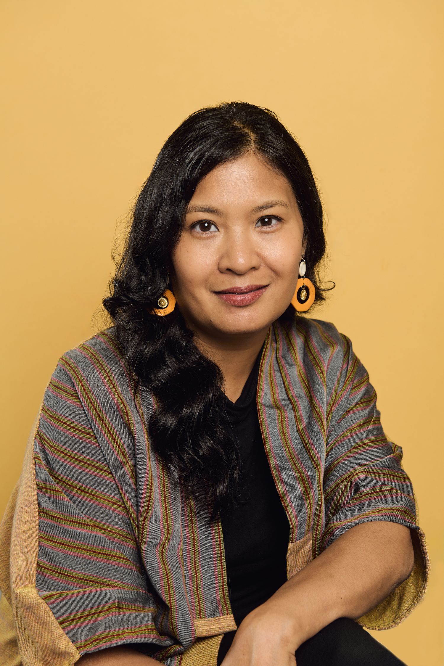 Portrait series against yellow background featuring casual business attire and gold hoop earrings.