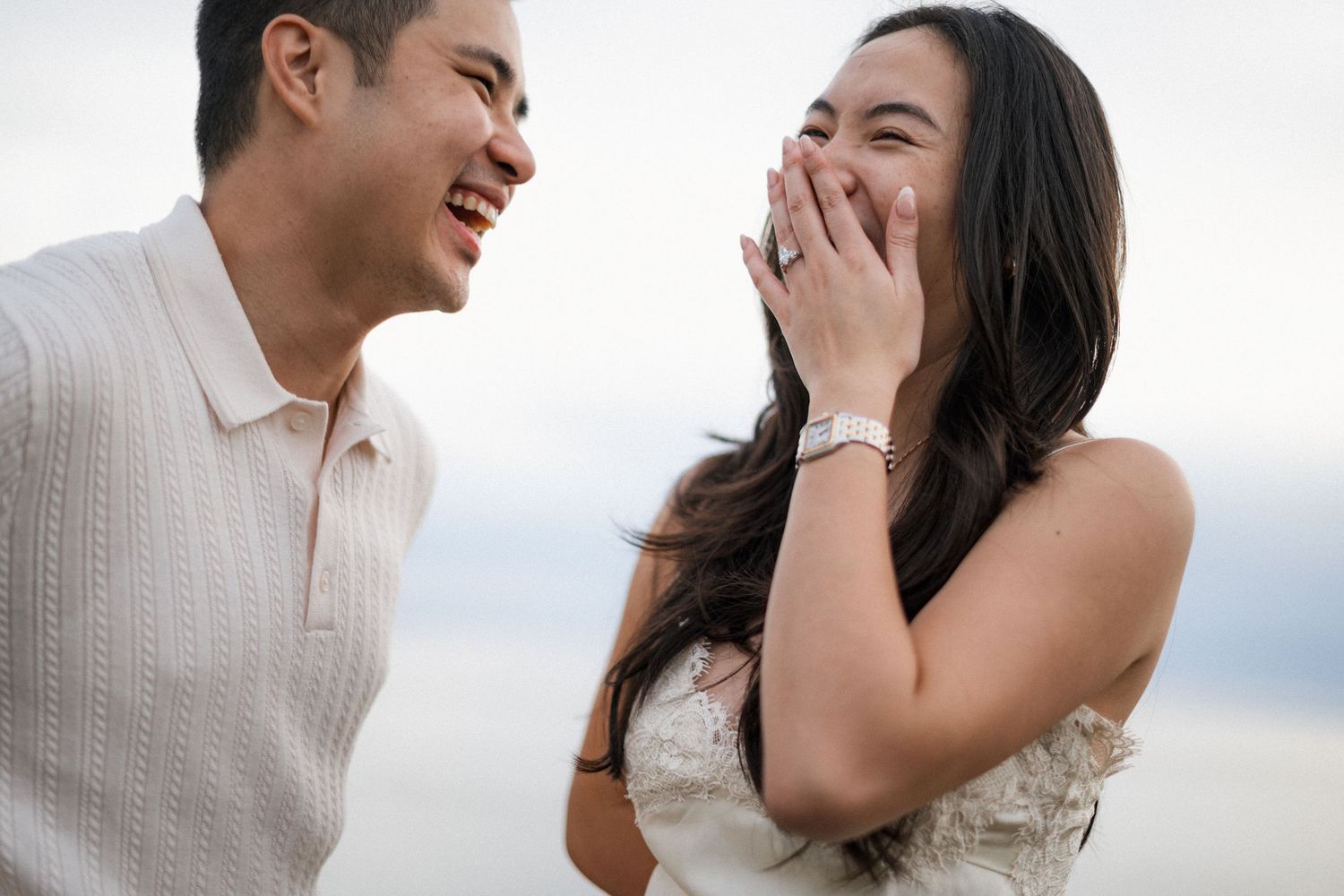 A couple shares joyful laughter during their engagement photoshoot on a bright, airy backdrop.