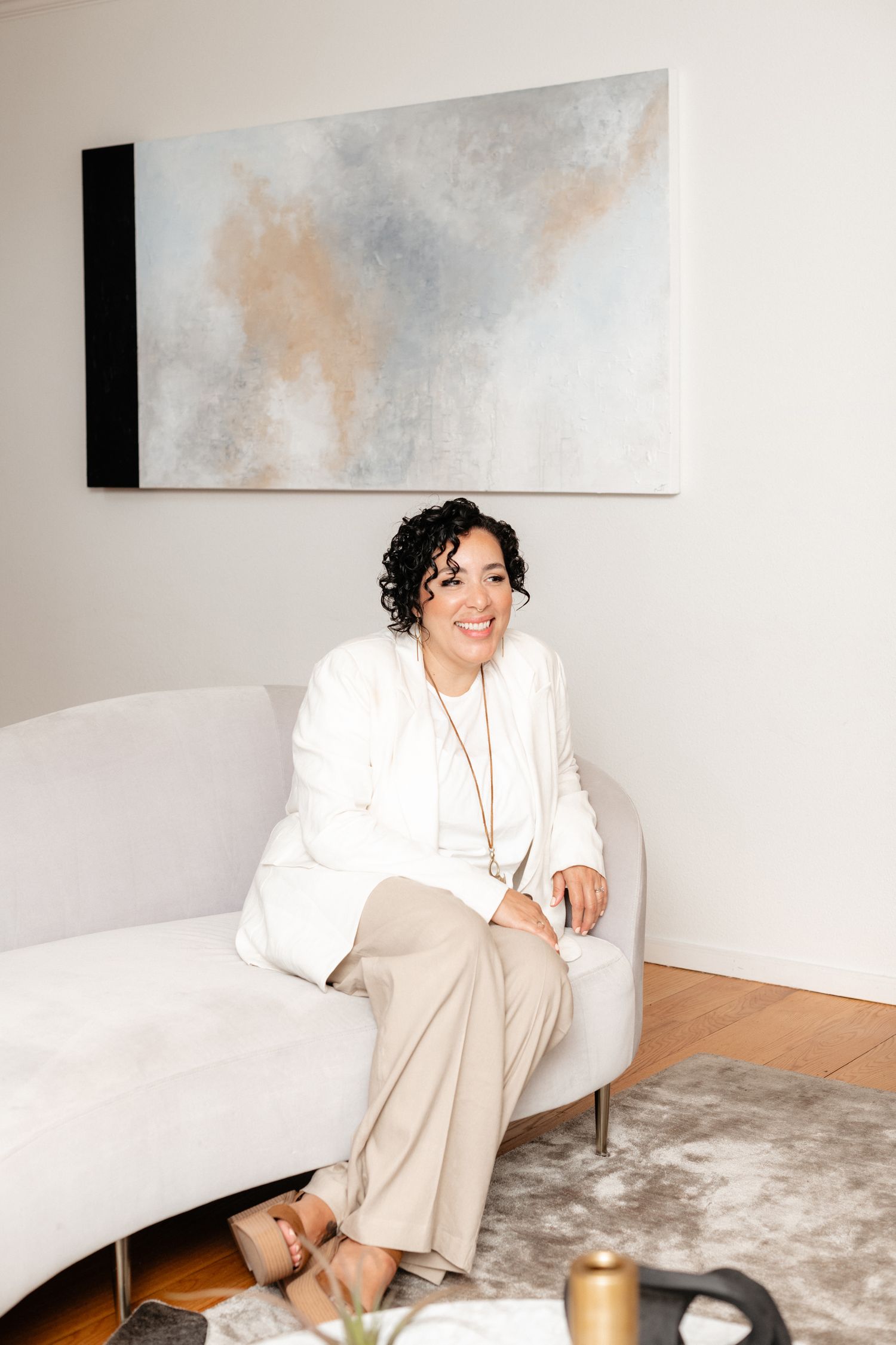 Lifestyle portraits of someone relaxing on a couch in a minimalist white room with abstract wall art.