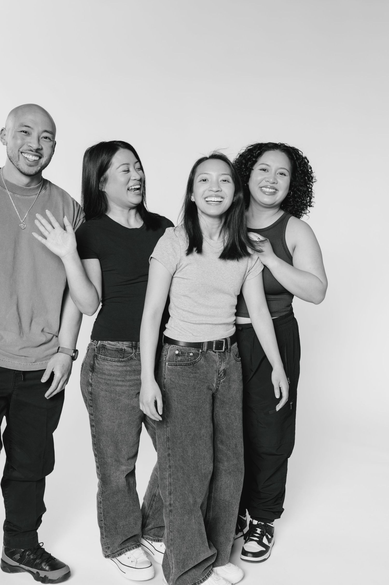 Black and white photo of four smiling young Asian adults posing together in casual outfits against a white background.