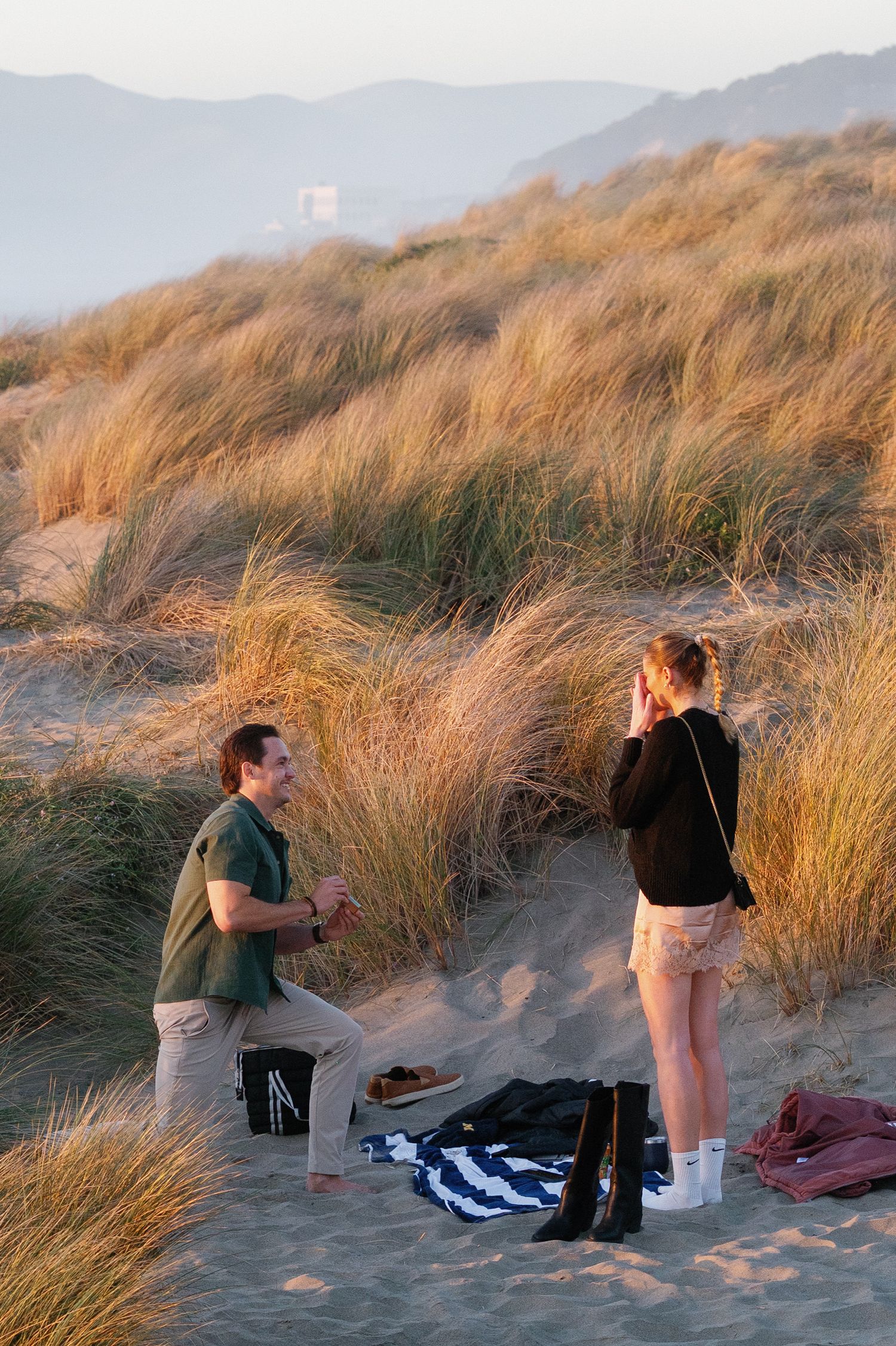 Emotional beach proposal scene with couple among sand dunes at sunset.