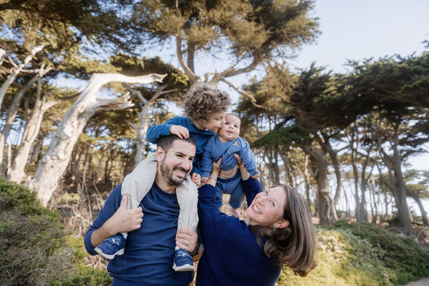 Playful family moments captured in a forest setting with sunlight filtering through trees.
