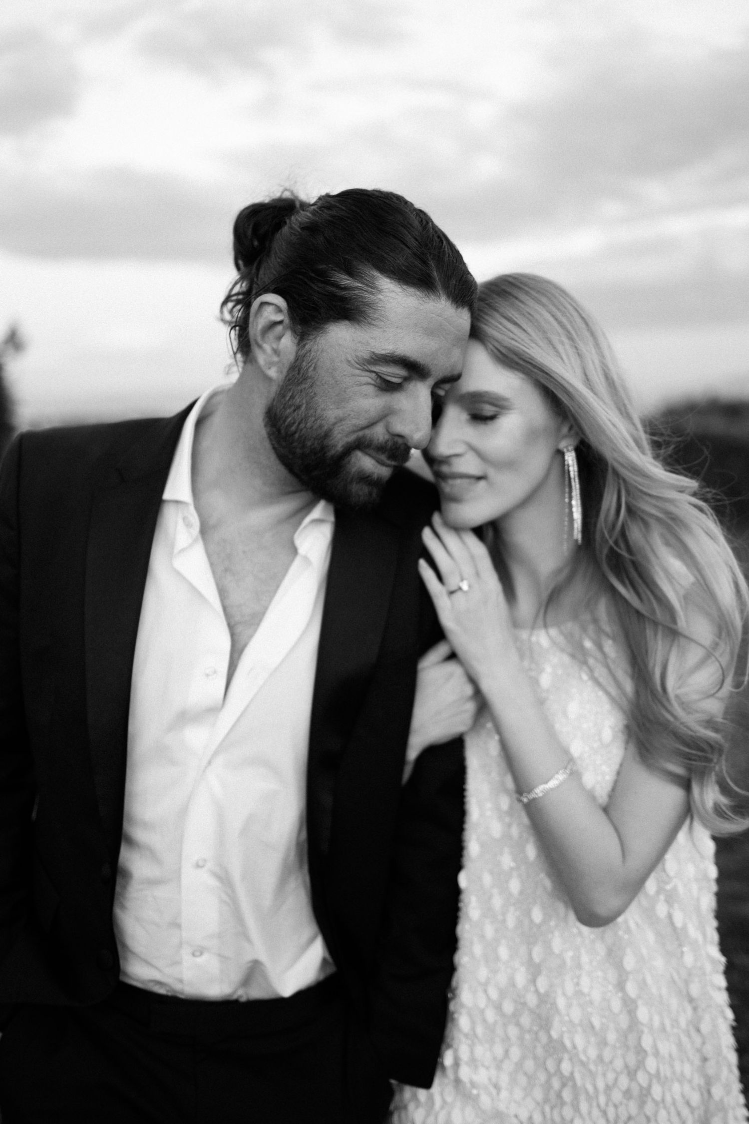 Intimate black and white portrait of a couple sharing a tender moment outdoors under cloudy skies. Surprise proposal in Cefalù.