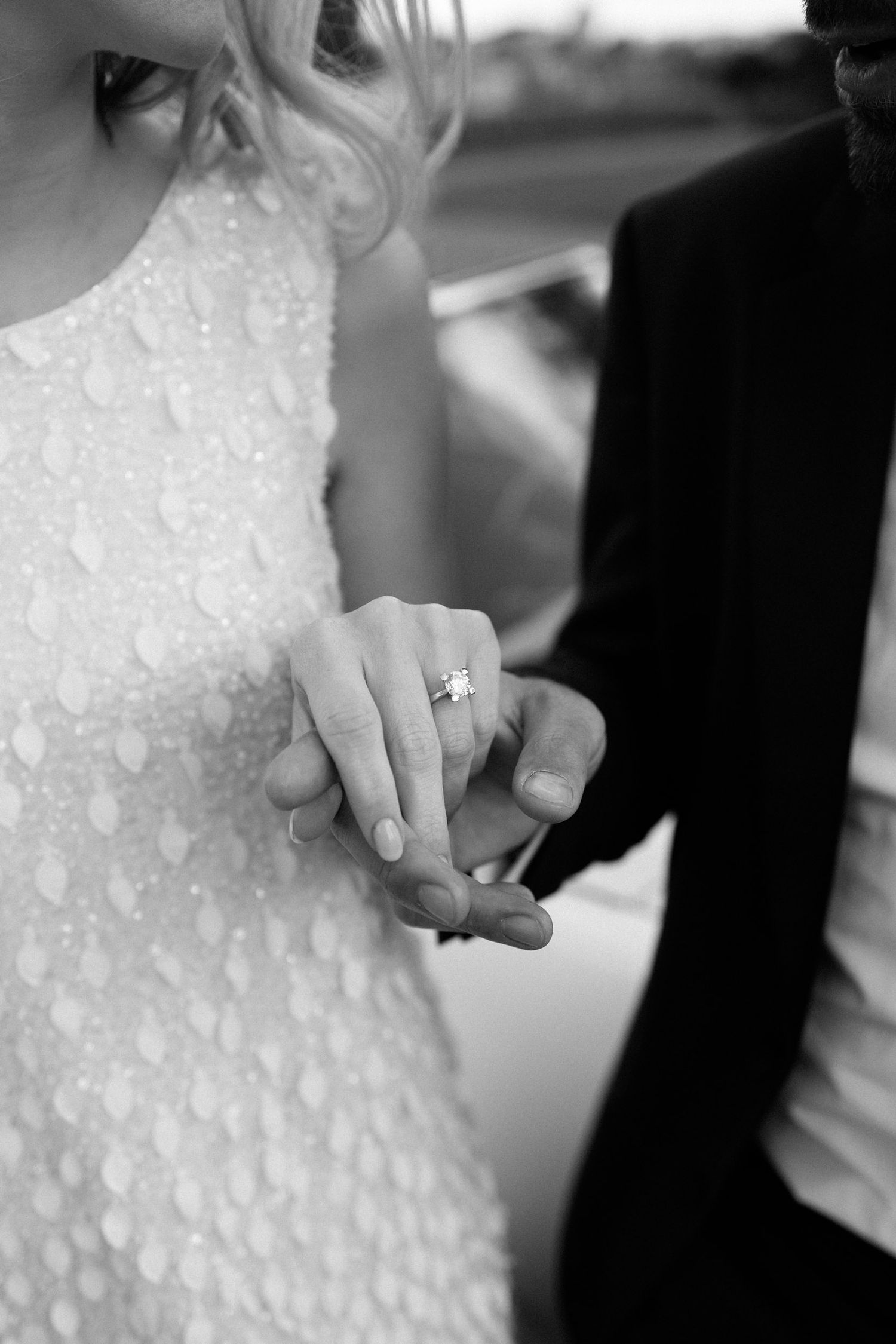 A close-up black and white photo shows hands clasped together with a wedding proposal ring visible on the bride's finger.