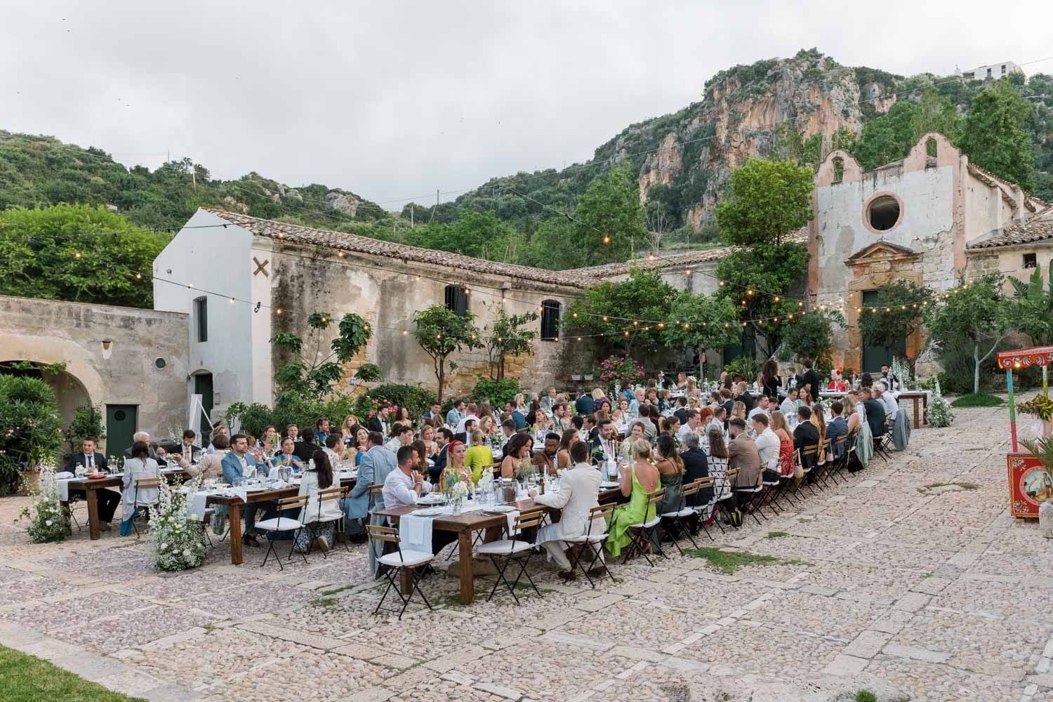 Outdoor wedding reception in rustic Italian courtyard with long tables. Wedding at Tonnara di Scopello in Sicily.