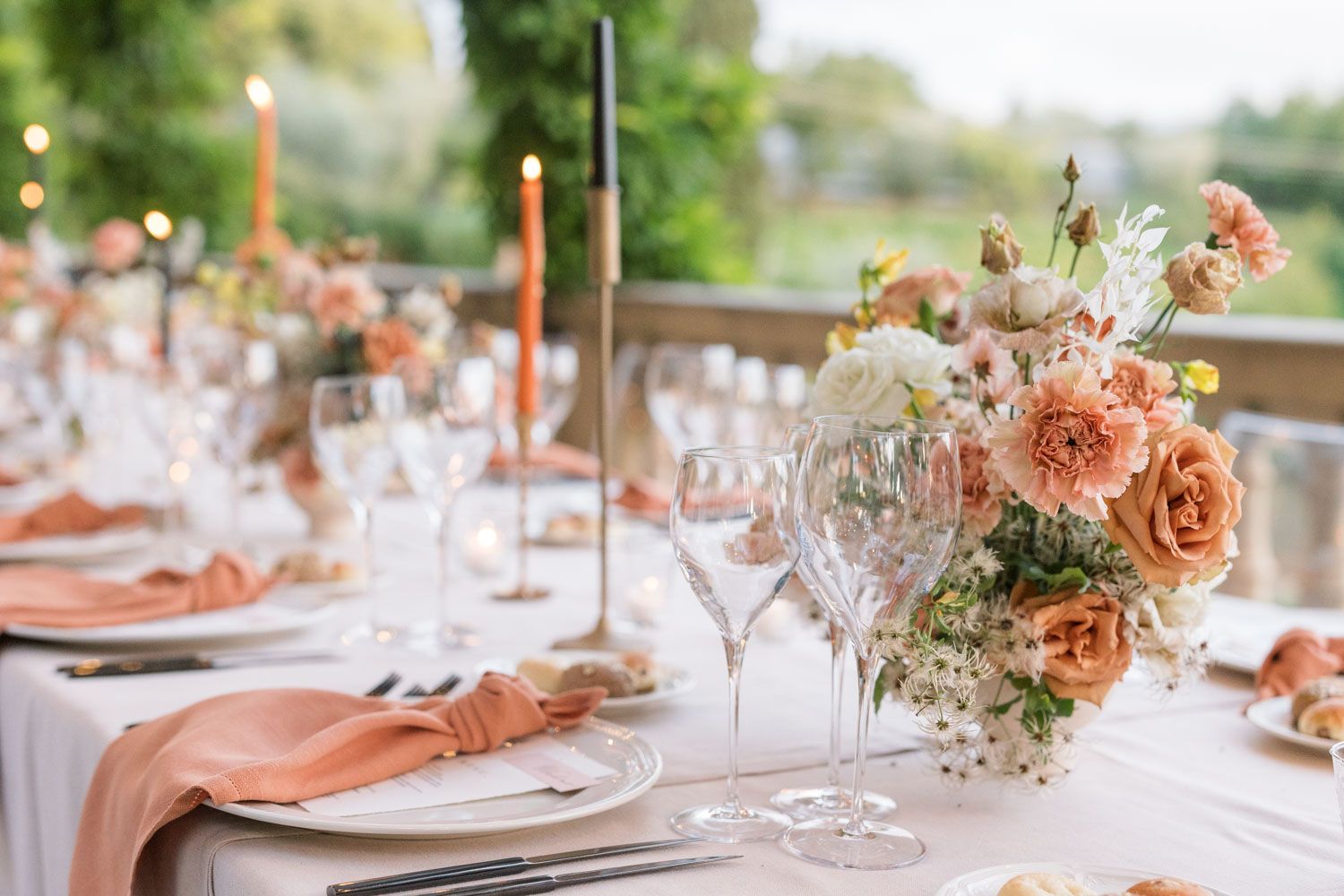 Elegant wedding table setting with peach roses, crystal glasses, candles, and salmon napkins at an outdoor venue in Sicily