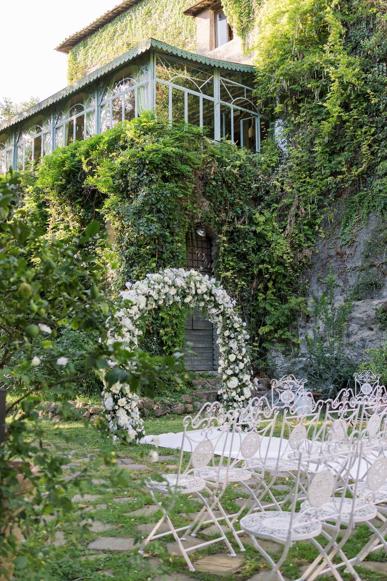 Wedding ceremony setup with white chairs and floral arch at Castello di Tor Crescenza, Rome.