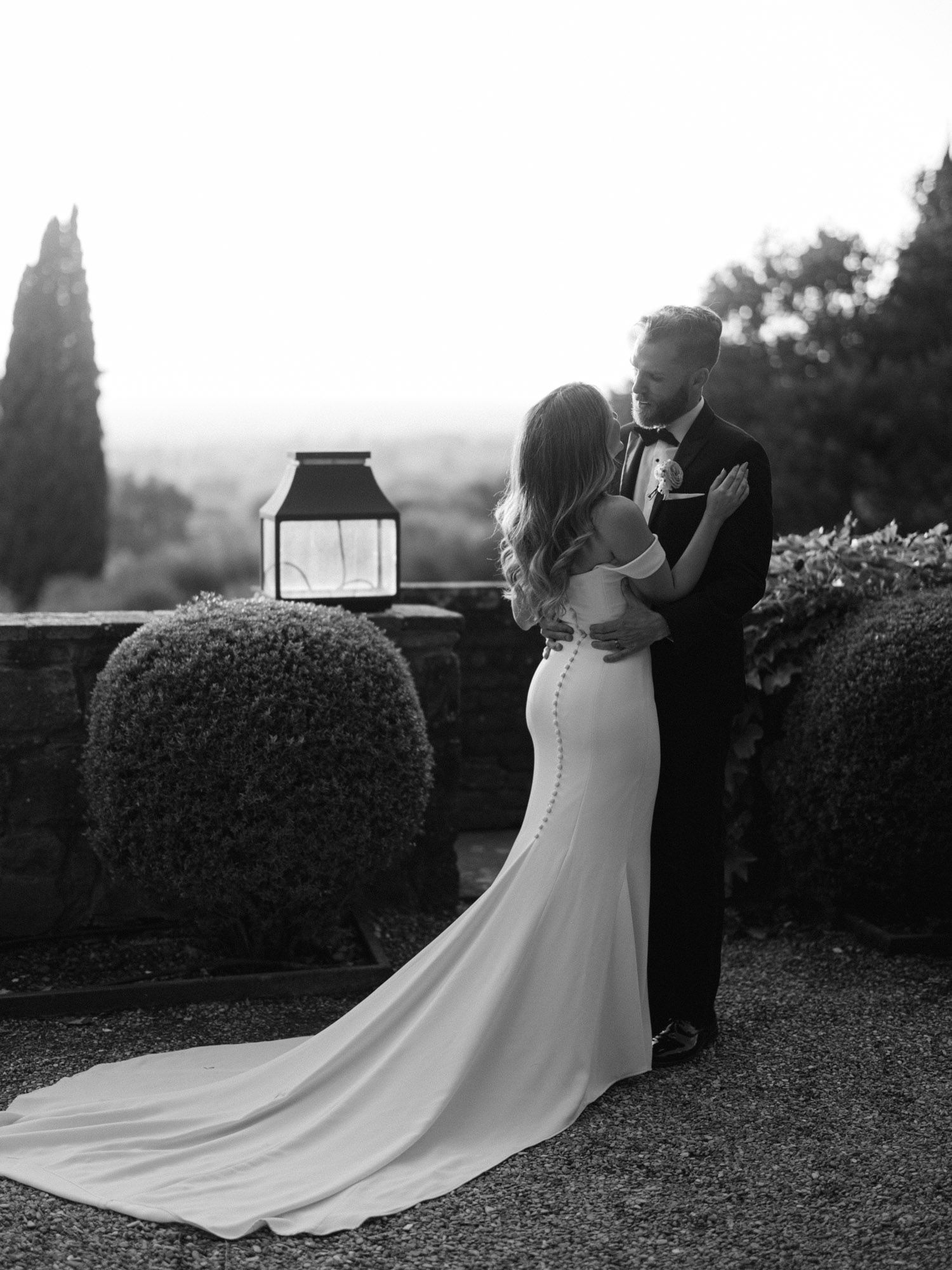 Wedding couple embracing at Villa Le Fontanelle in Florence, bride seen from behind with elegant gown during destination wedding in Italy.