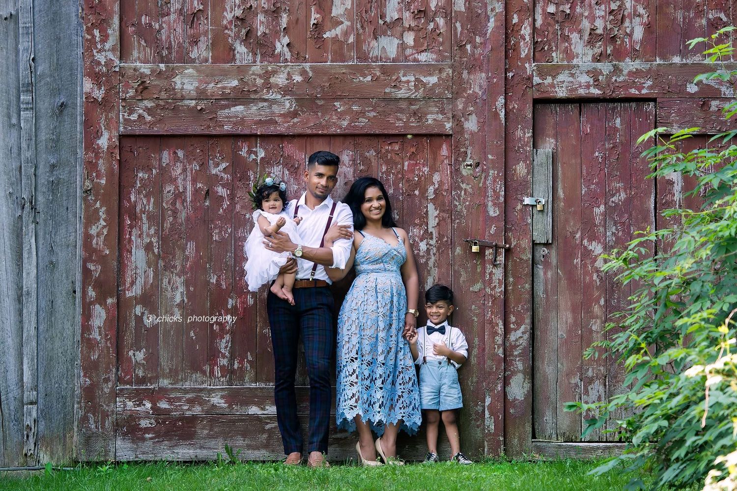 Family of four posing in front of rustic red barn doors.