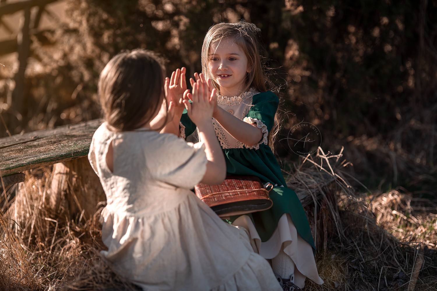 Two young girls in vintage dresses playing clapping games together in a golden outdoor setting.