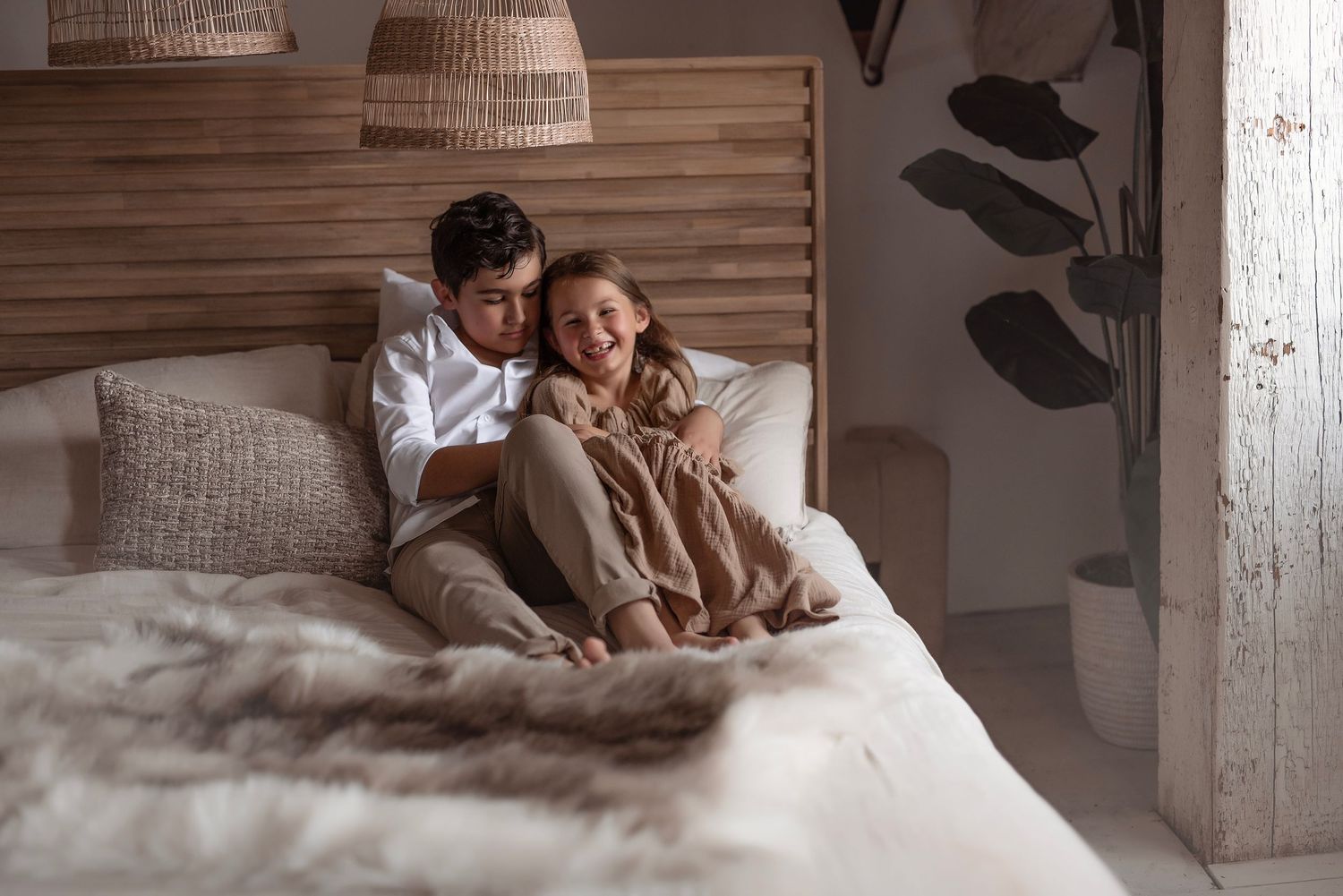 Couple smiling and cuddling together on cozy bed in warm bohemian bedroom interior.