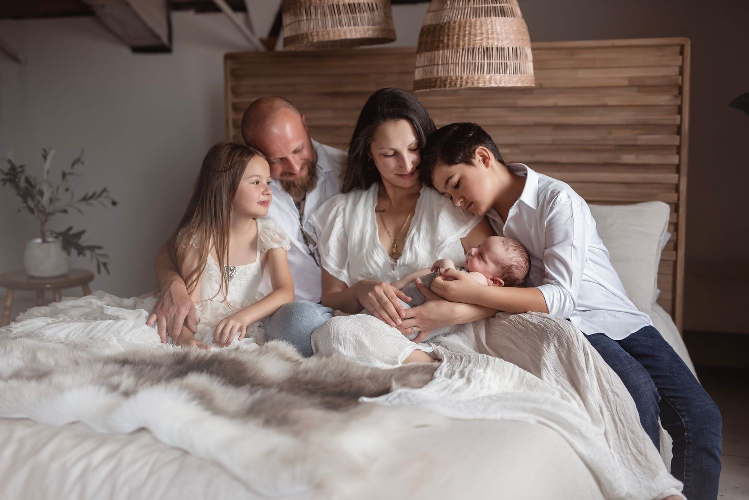 Happy family of five gathered on a white bed admiring their precious newborn baby together at home.