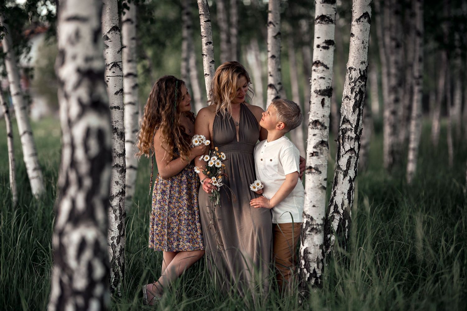 Pregnant woman with daughter and son in birch forest with flowers.