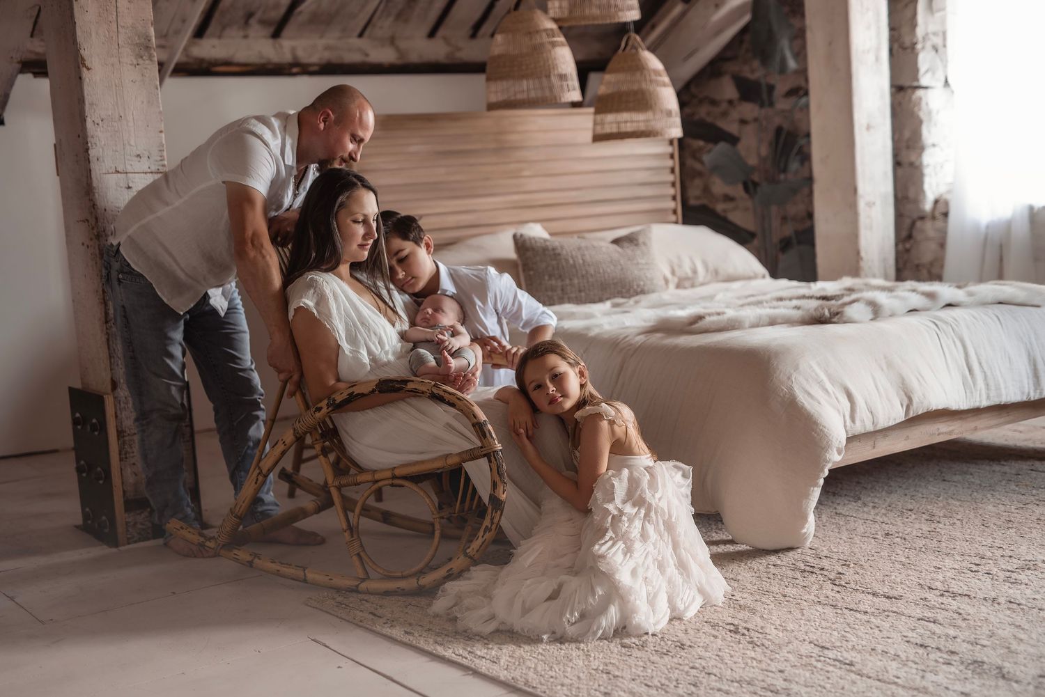Happy family with newborn baby posing in rustic bedroom with wooden accents and rattan chair.