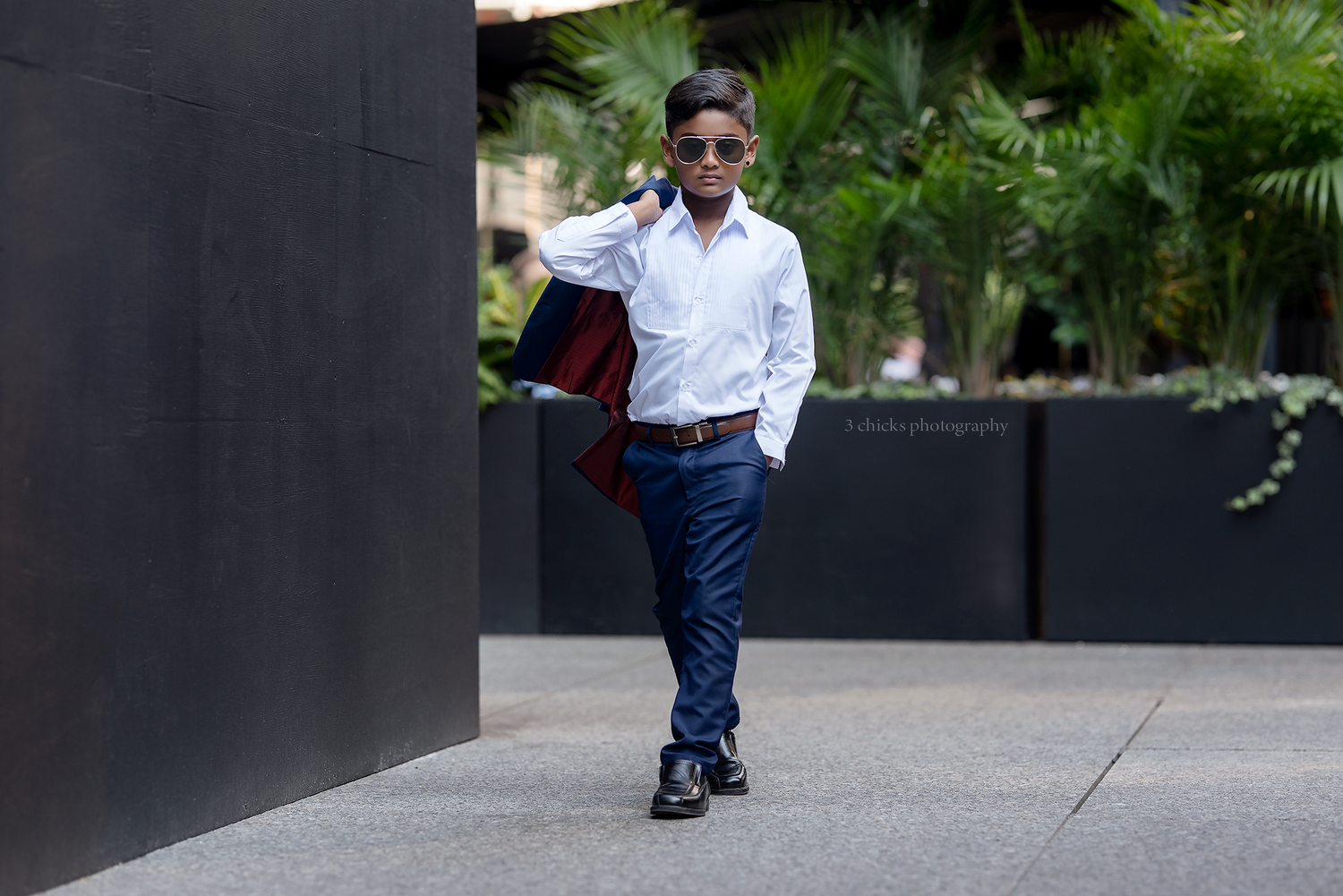 Young boy in white shirt and blue pants walking confidently in an outdoor urban setting.