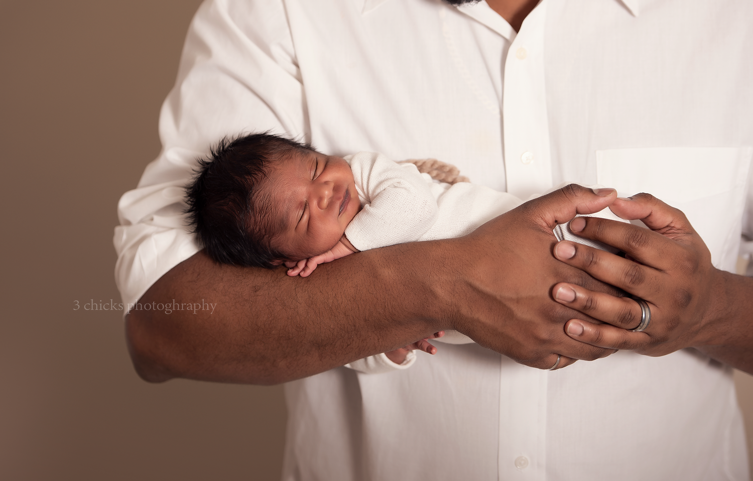 A father in a white shirt cradles a sleeping newborn baby in his arms, showcasing a tender parenting moment.