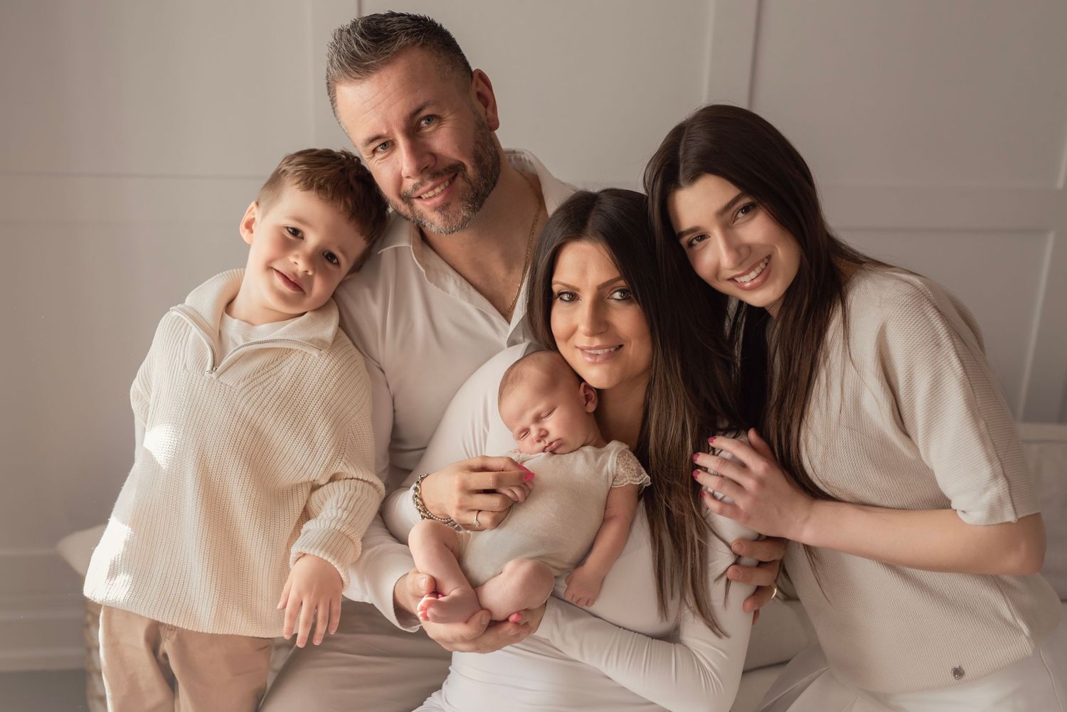 Happy family of five in matching cream outfits posing together, parents holding newborn baby with two older children.