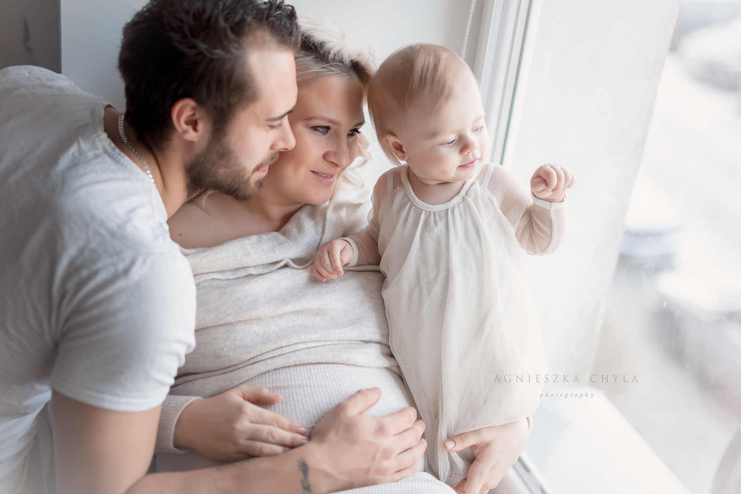 Happy family with parents and baby by window in bright room.