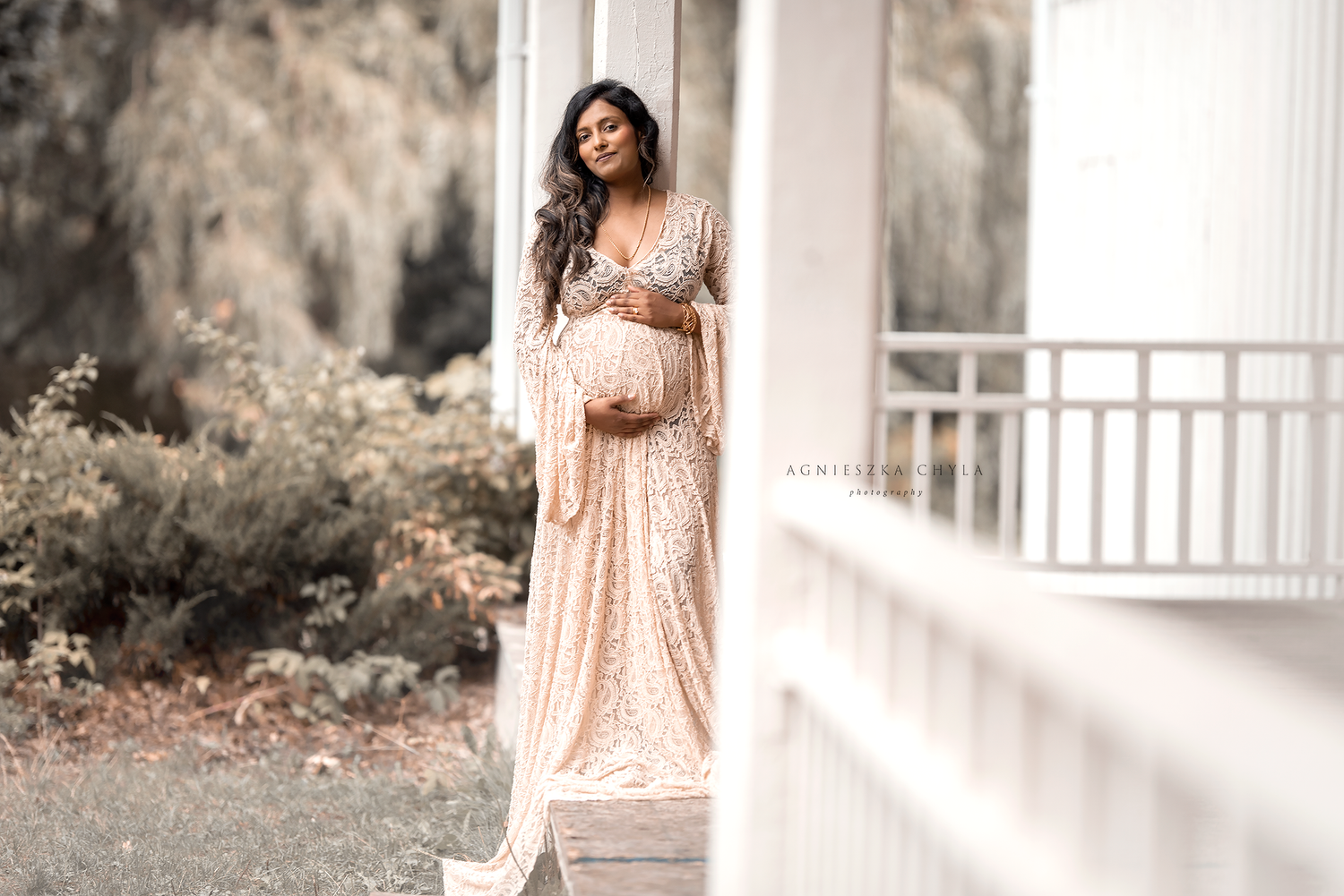 Pregnant woman in a sequined blush gown posing on a porch, cradling her baby bump during a maternity photo shoot.