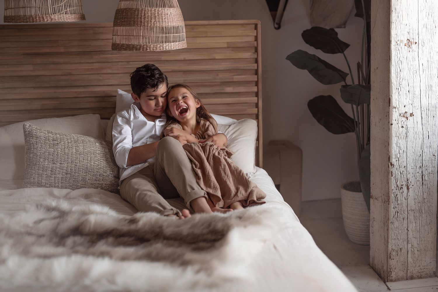 Playful couple laughing and relaxing on bed in cozy boho-style bedroom with natural decor.