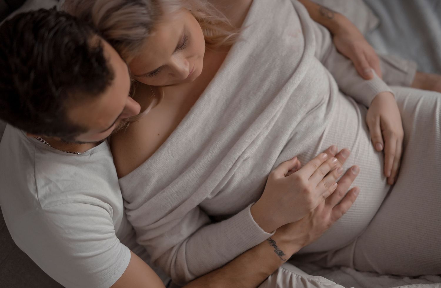 Loving couple embracing pregnant belly together on bed.