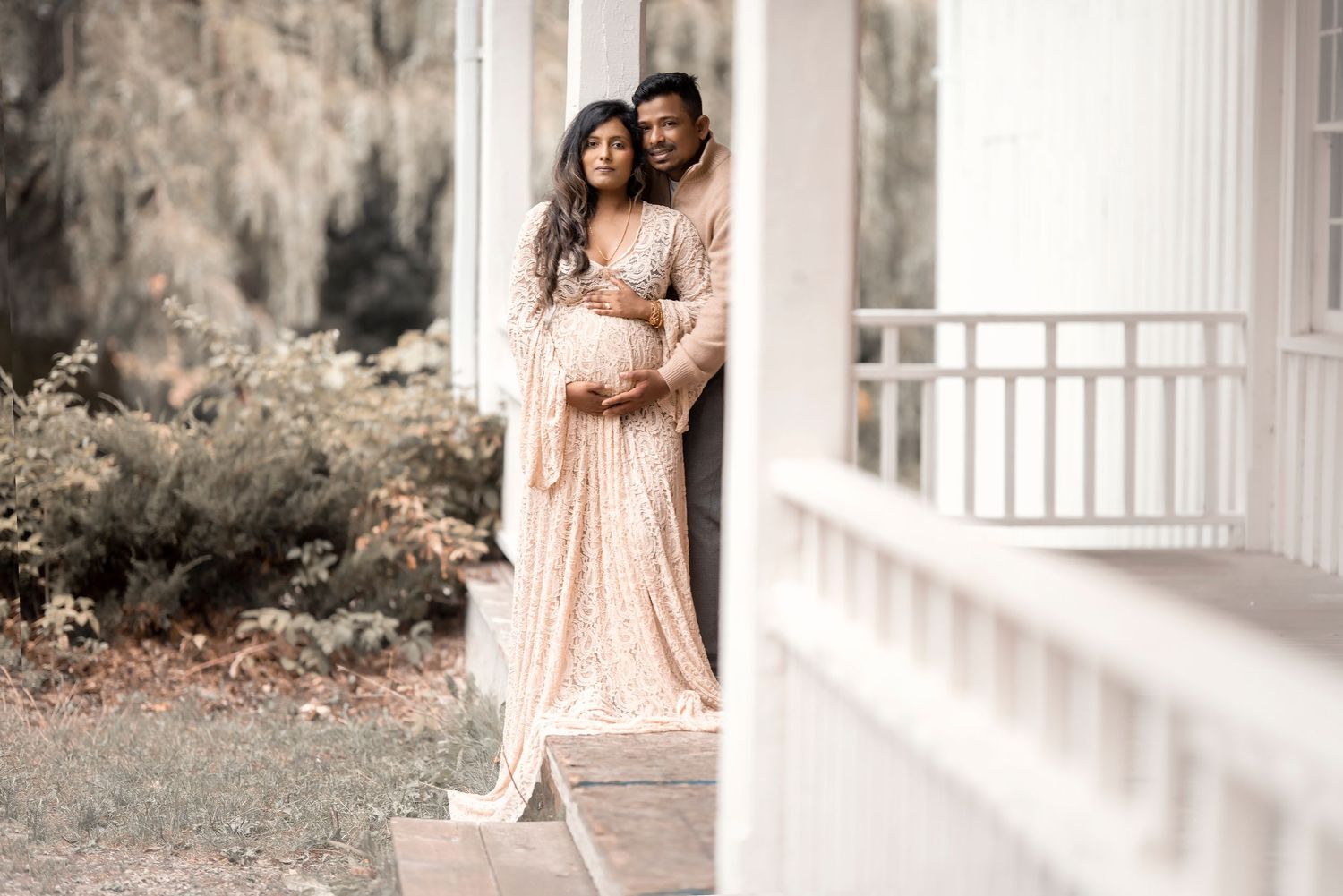 Couple in matching beige outfits sharing a tender maternity portrait on porch.
