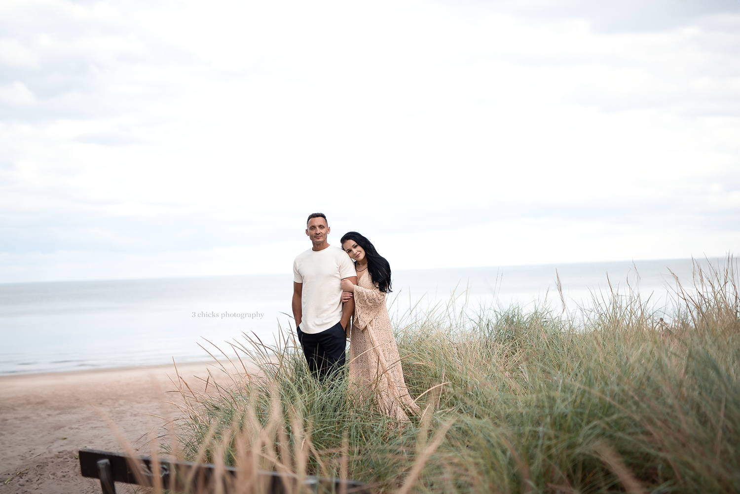 Couple standing together on sandy beach dunes with ocean backdrop on a cloudy day. Couple photography Vaughan