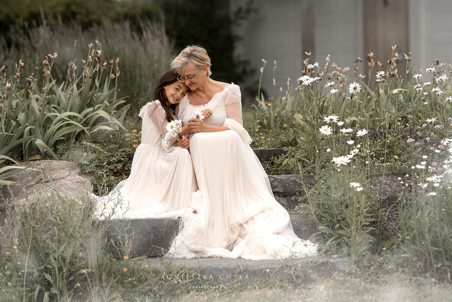 Mother and daughter in white dresses sharing tender moment on garden steps.
