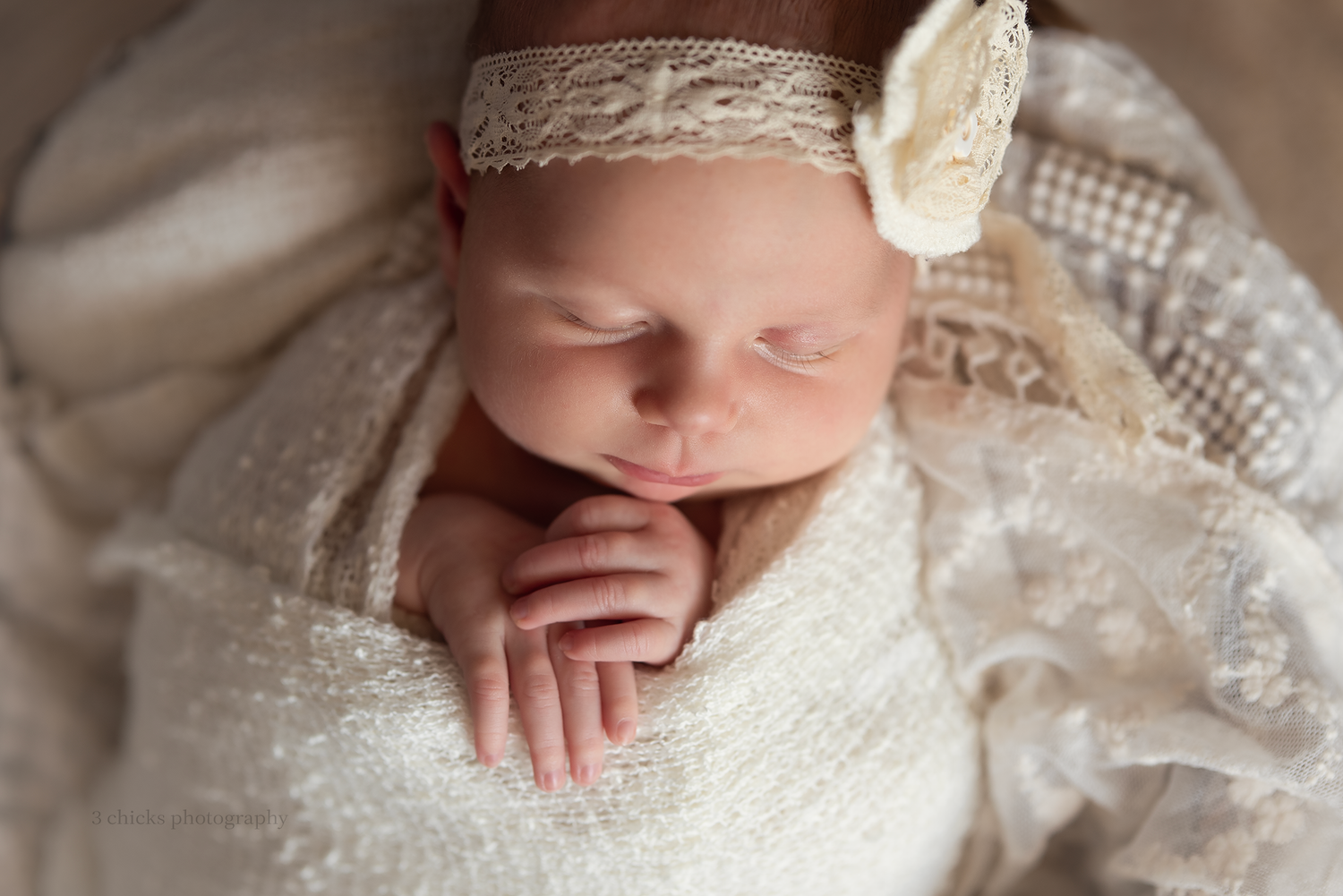 Newborn baby girl sleeping peacefully wrapped in white lace with a delicate floral headband.