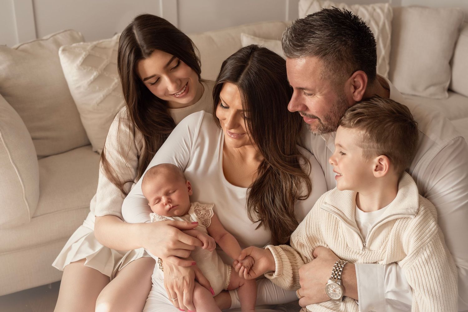 Family of five gathered on a couch, parents admiring their newborn baby with two older children beside them.