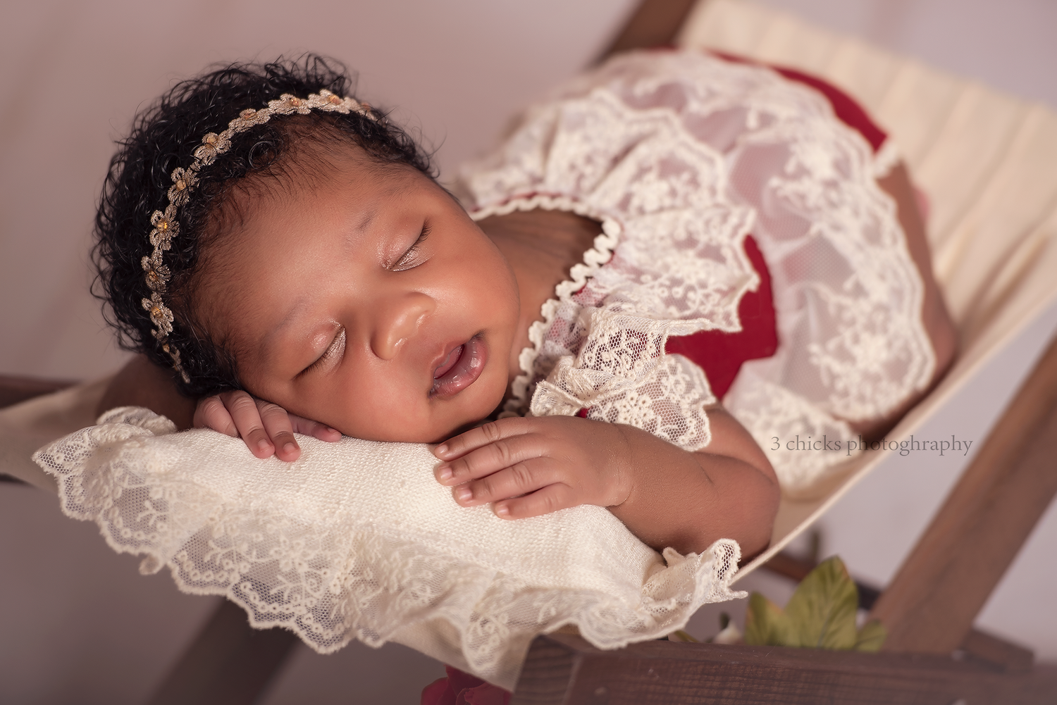 Sleeping newborn baby girl in white lace dress and gold headband resting peacefully in a wooden crib.