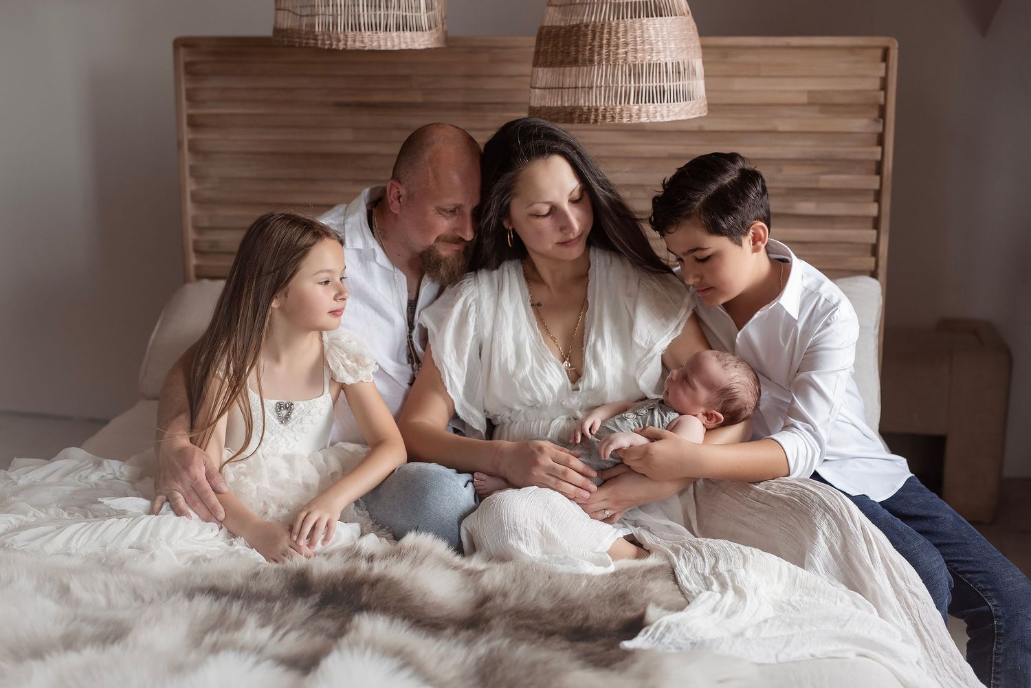 Family of five with newborn baby gathered together on a cozy bed indoors.