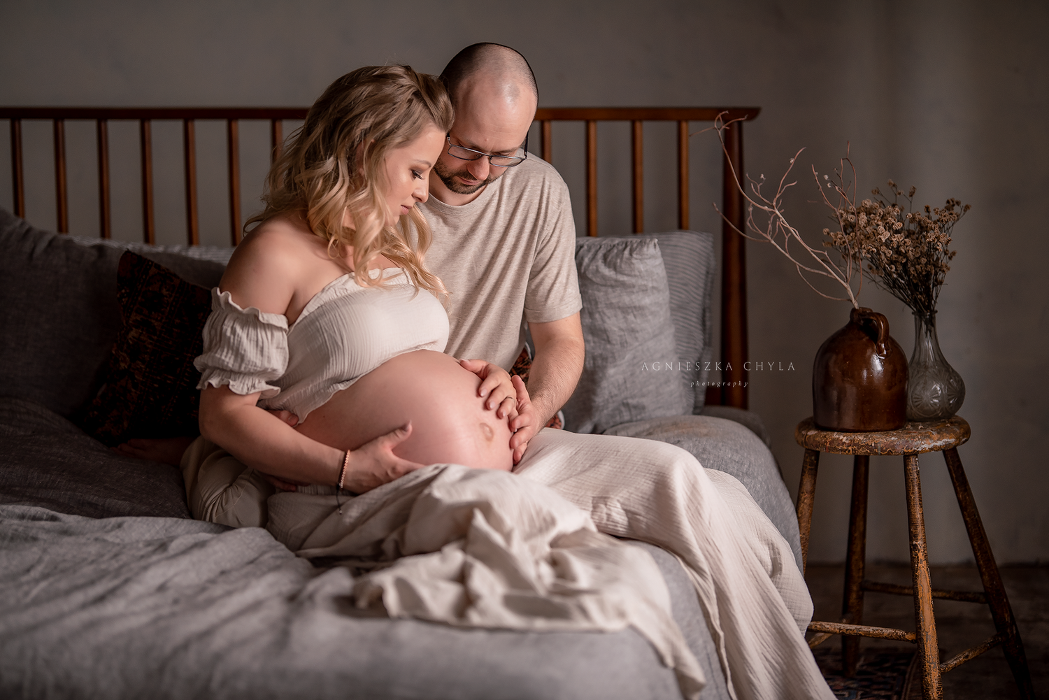 Expecting couple sitting on bed tenderly looking at pregnant belly during maternity photo session.