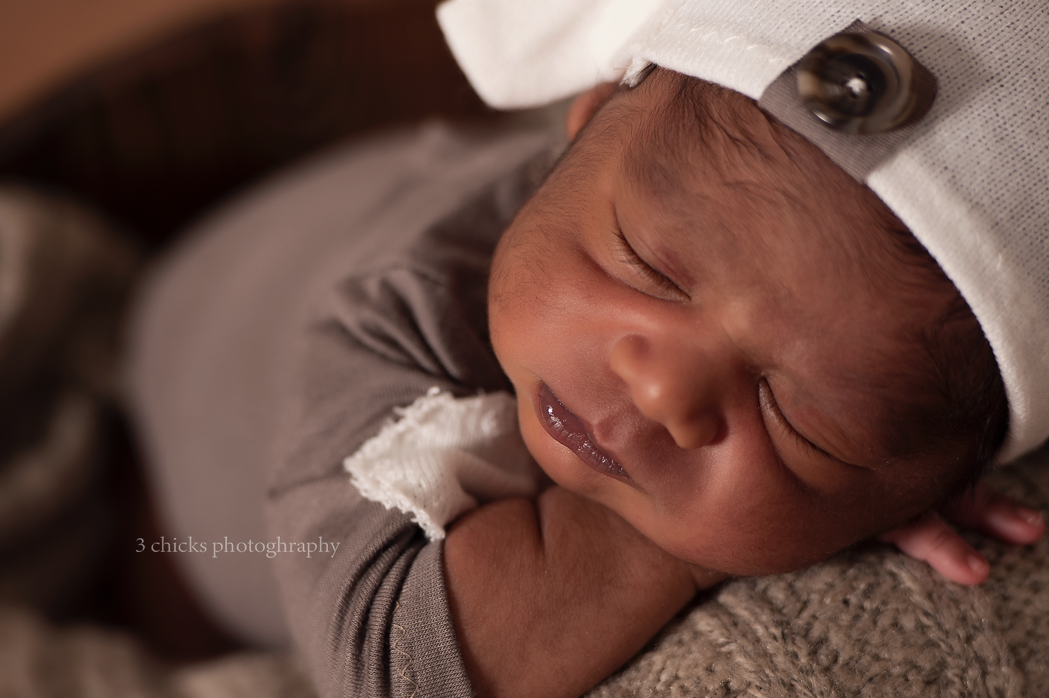 Peaceful newborn baby sleeping in a cozy wrap wearing a white knit hat, captured in warm tones by 3 Clucks Photography.