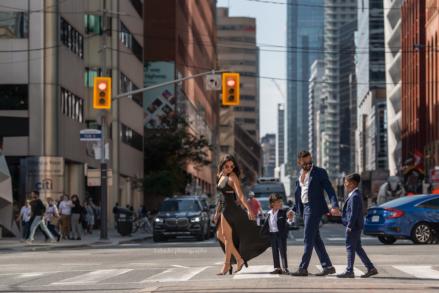 A stylish family crosses a busy urban street intersection in a vibrant city during daytime. Family photography session Milton