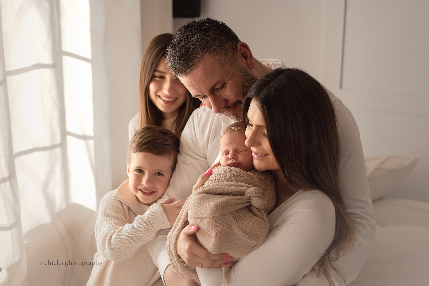 Family of four in white outfits lovingly gazing at newborn baby during professional newborn photography session.